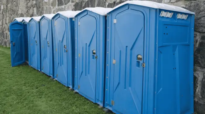 Row of blue portable toilets lined up on grass against a stone wall for event sanitation in Atlanta, GA