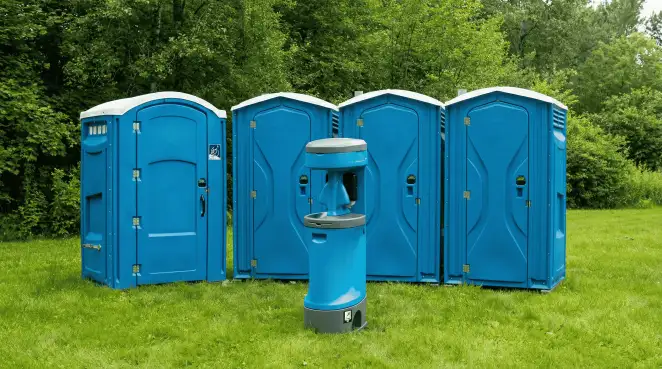 Four blue portable toilets and a matching hand washing station on grass near trees, a common sight at local outdoor events in Atlanta, GA